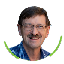 A middle-aged man with a mustache, wearing glasses and a plaid shirt, smiling in front of a blue background, framed by a green circular border.