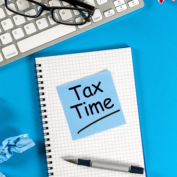 Top view of a desk with a notebook labeled "tax time", a keyboard, glasses, a pen, and crumpled paper on a blue background.