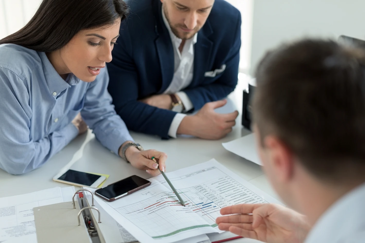 Three business professionals analyzing a document with charts together at a table in a well-lit office.