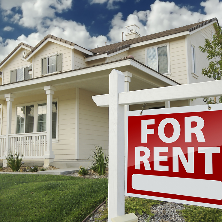 A "for rent" sign in front of a spacious two-story house with a well-manicured lawn.