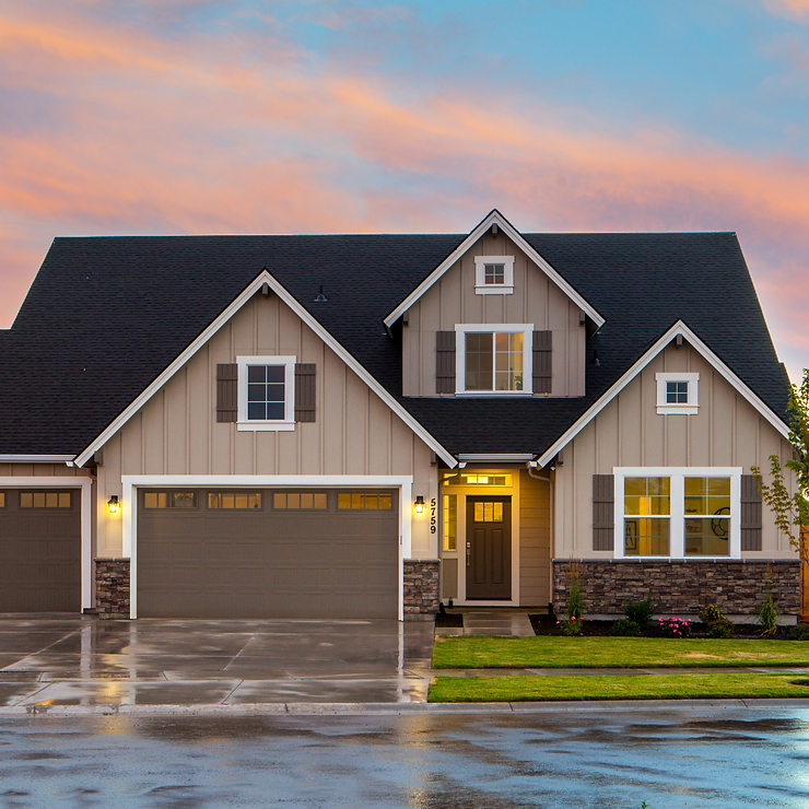 A two-story suburban house with a beige exterior and two garage doors, showcased under a sunset sky.