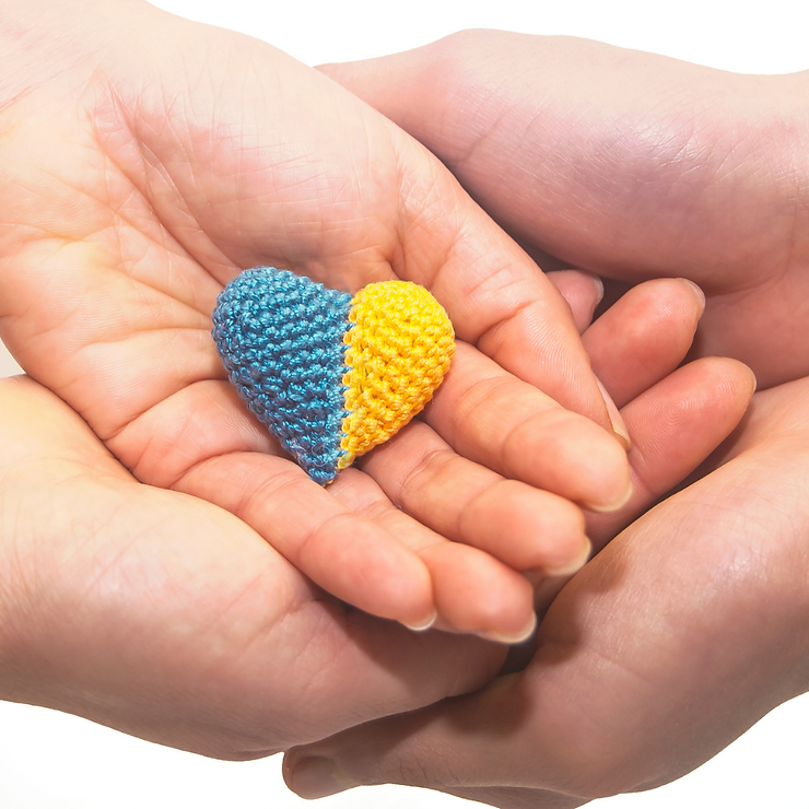 Two hands cradling a crocheted heart divided into blue and yellow halves, symbolizing support for ukraine.