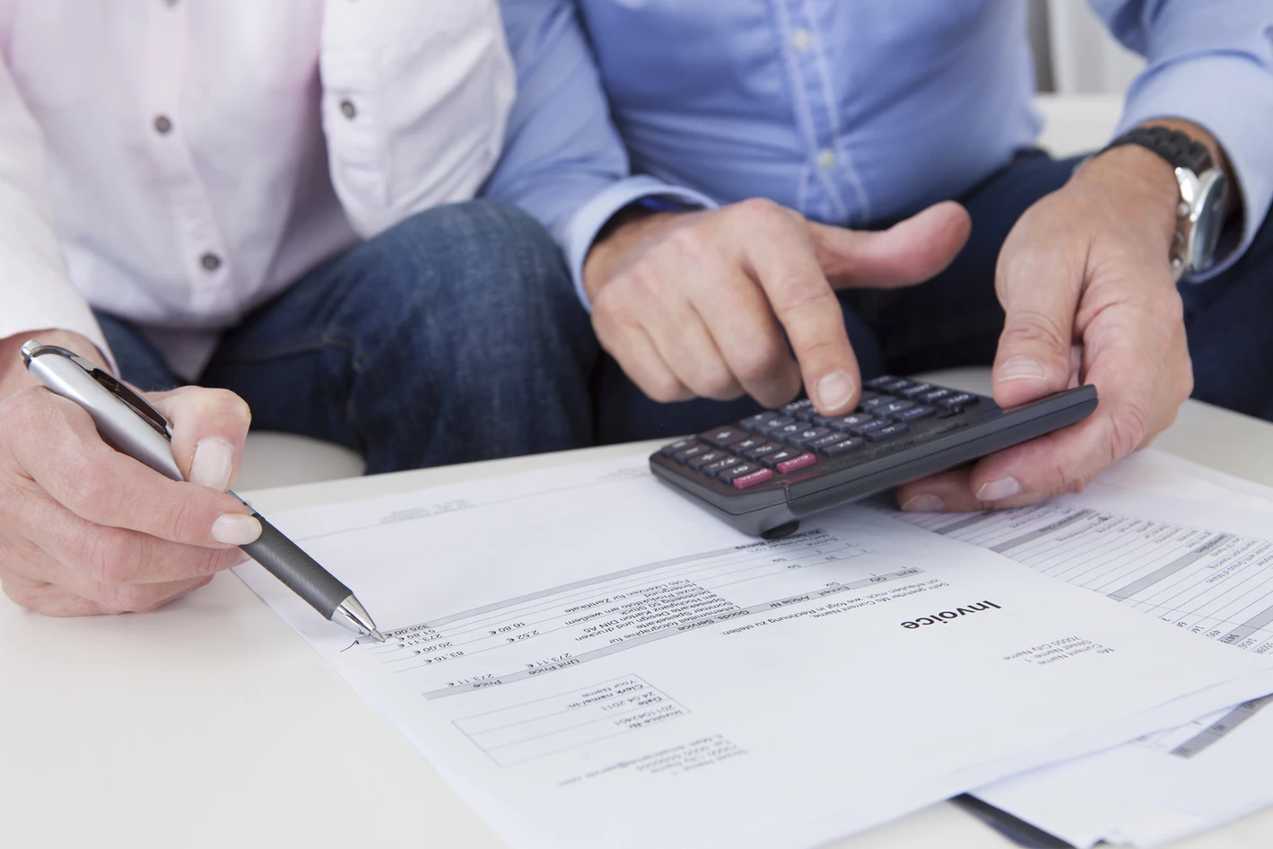 Two people discussing financial documents at a desk, one using a calculator and the other holding a pen.