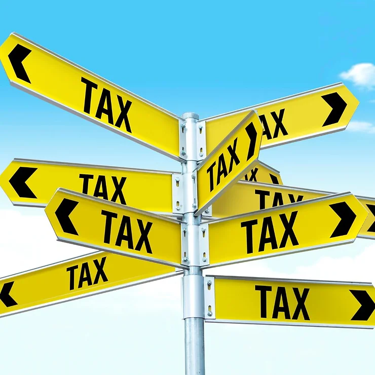 Multiple yellow directional signs labeled "tax" pointing in various directions on a metal pole against a partly cloudy sky.