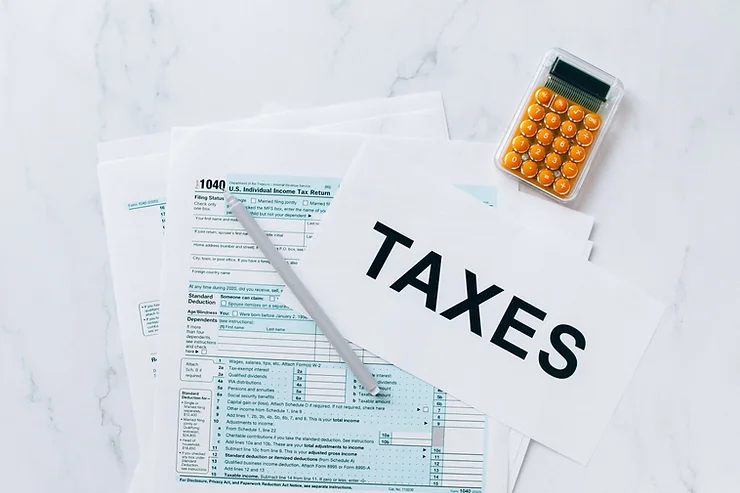 A selection of tax forms, a calculator, and a paper labeled "taxes" on a marble surface.