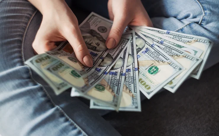 A person's hands holding and fanning out multiple us dollar bills.