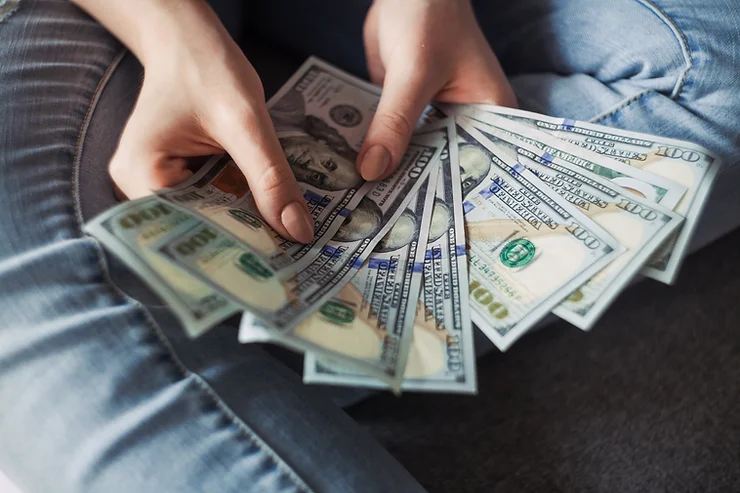 A person's hands holding and fanning out multiple us dollar bills.