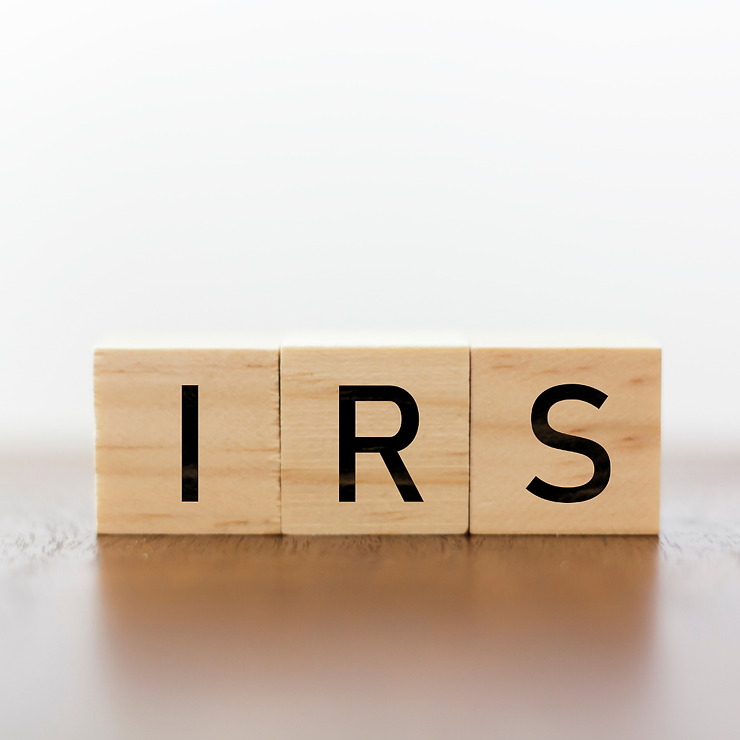 Wooden blocks spelling out "irs" on a reflective surface with a blurred background.