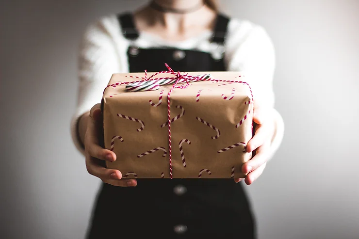 A person holding a wrapped gift with a red and white string bow, focusing on the packaged present against a blurred background.