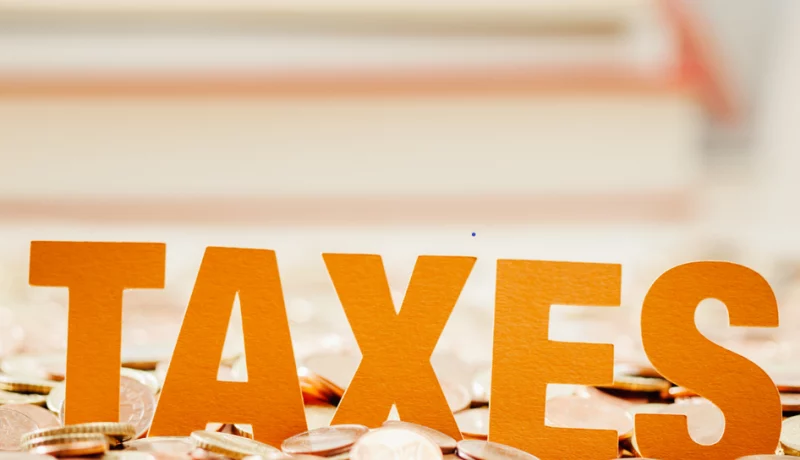 The word "taxes" in bold orange letters against a backdrop of scattered coins, focusing on financial themes.