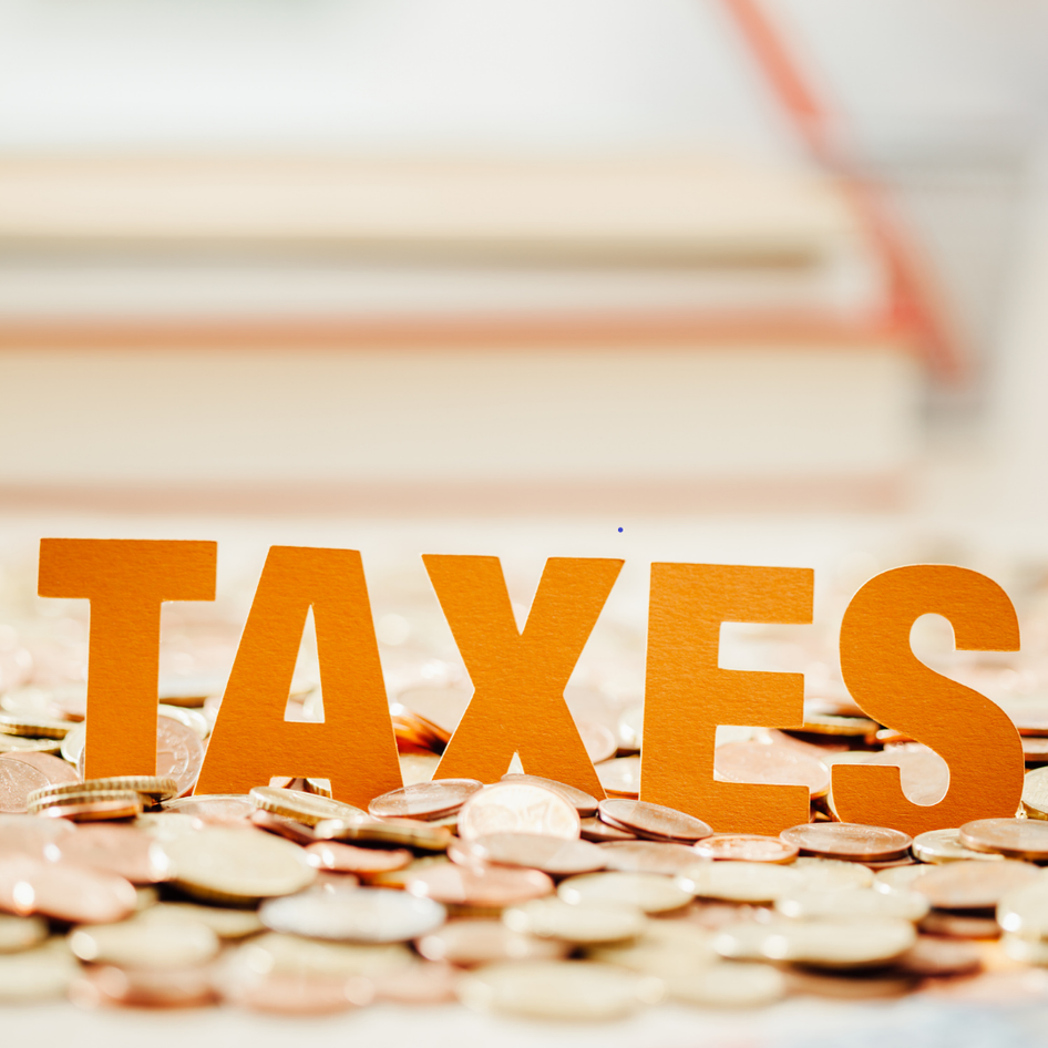 The word "taxes" in bold orange letters against a backdrop of scattered coins, focusing on financial themes.