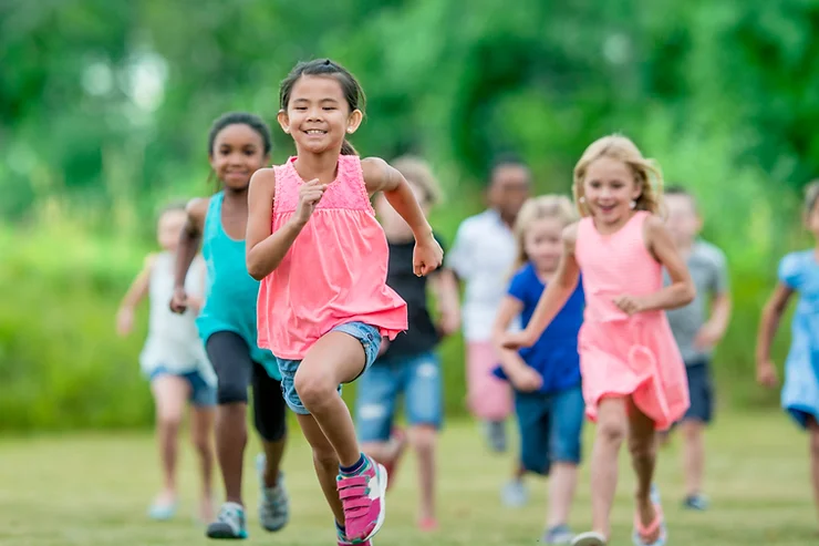 A group of diverse children happily racing in a grassy field, with a young girl in pink leading the way.