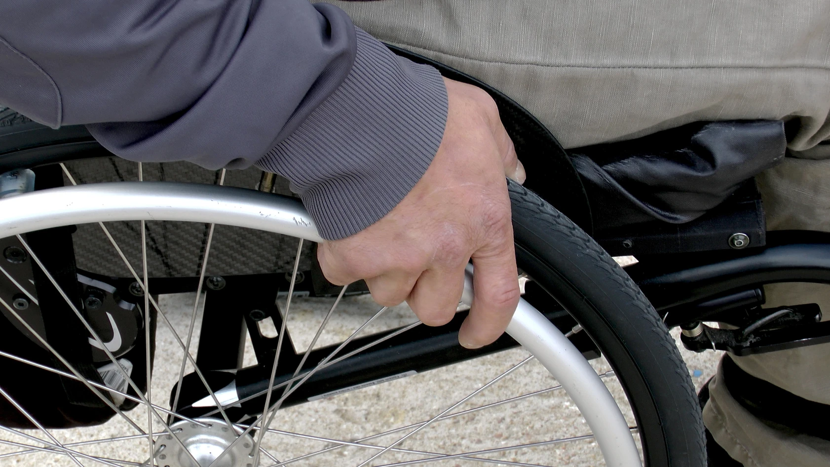 A close-up of a person's hand pressing on the tire of a wheelchair, indicating either movement initiation or a brake check