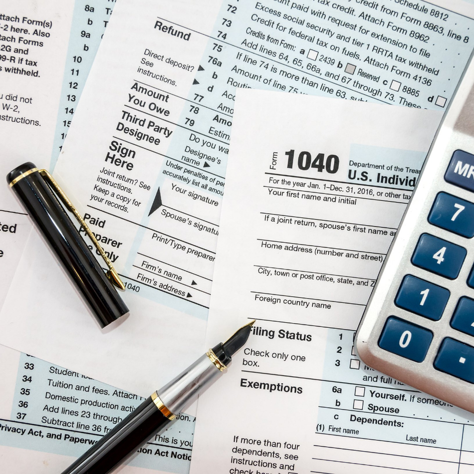 A calculator, two pens, and a tax form on a desk, symbolizing financial planning or tax calculation.