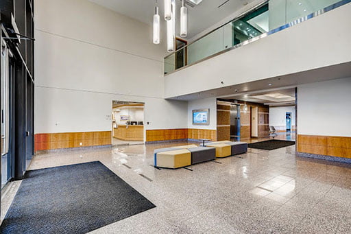 Modern office lobby with sleek furniture, pendant lighting, and polished stone flooring, featuring a reception desk in the background.