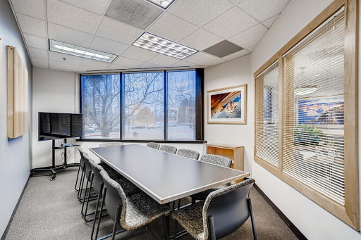 Bright conference room with a long table, several chairs, a tv on the wall, snowy view outside large windows, and artwork on the walls.