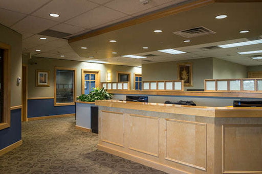 Interior of an office lobby with wooden counters, carpeted floors, wall art, and a potted plant.