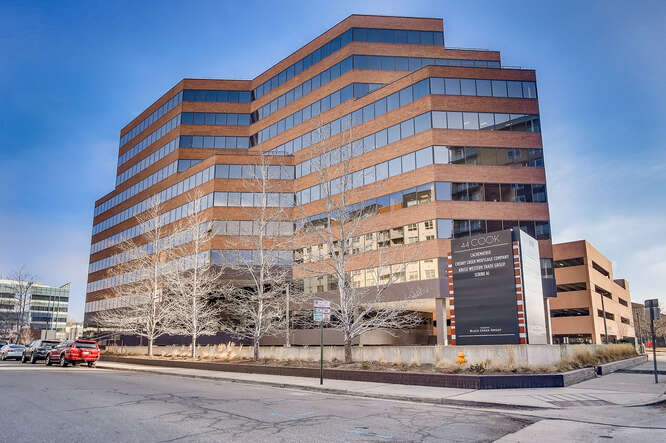 Modern multi-story office building with brown and orange facade, located on a city street with cars and bare trees under a clear sky.