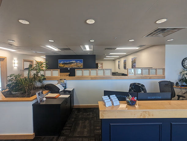 Modern office lobby with a reception desk, multiple pamphlets, plants, and a large scenic photograph on the wall.