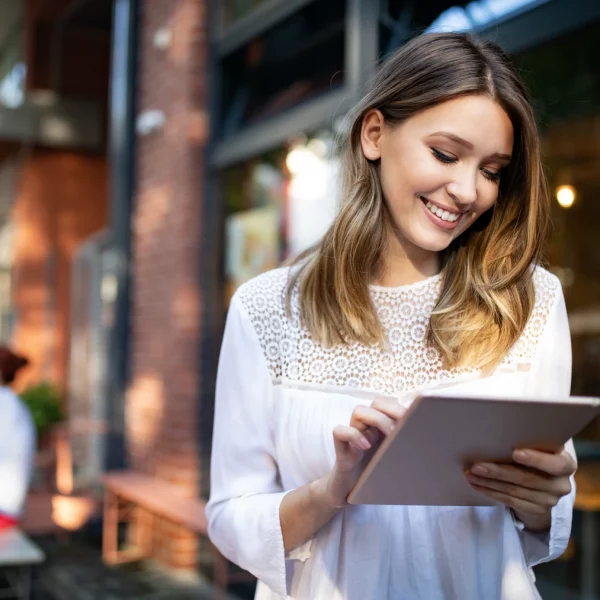 A smiling woman using a tablet outside a café looking for a bookkeeper in Littleton, CO.
